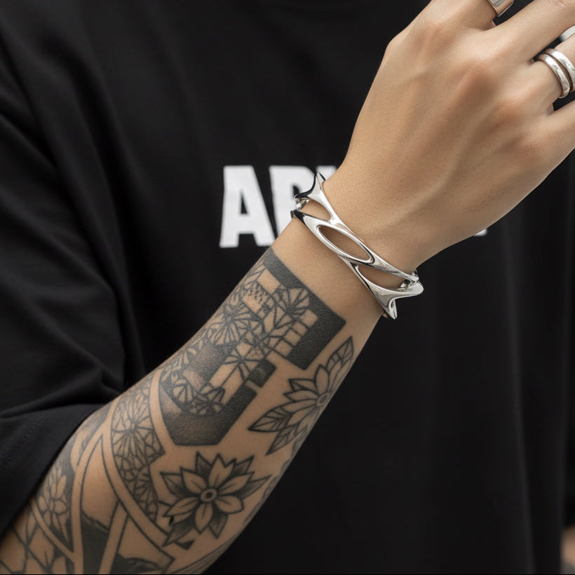 Person wearing a black t-shirt with visible branding, holding a phone with a silver bracelet and rings on a neutral background.