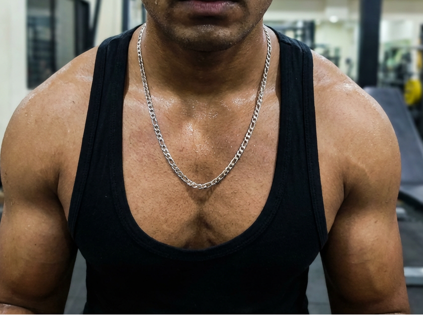 Man in a gym wearing a black tank top and chain necklace