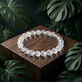 Clear beaded bracelet on a wooden block with green leaves in the background