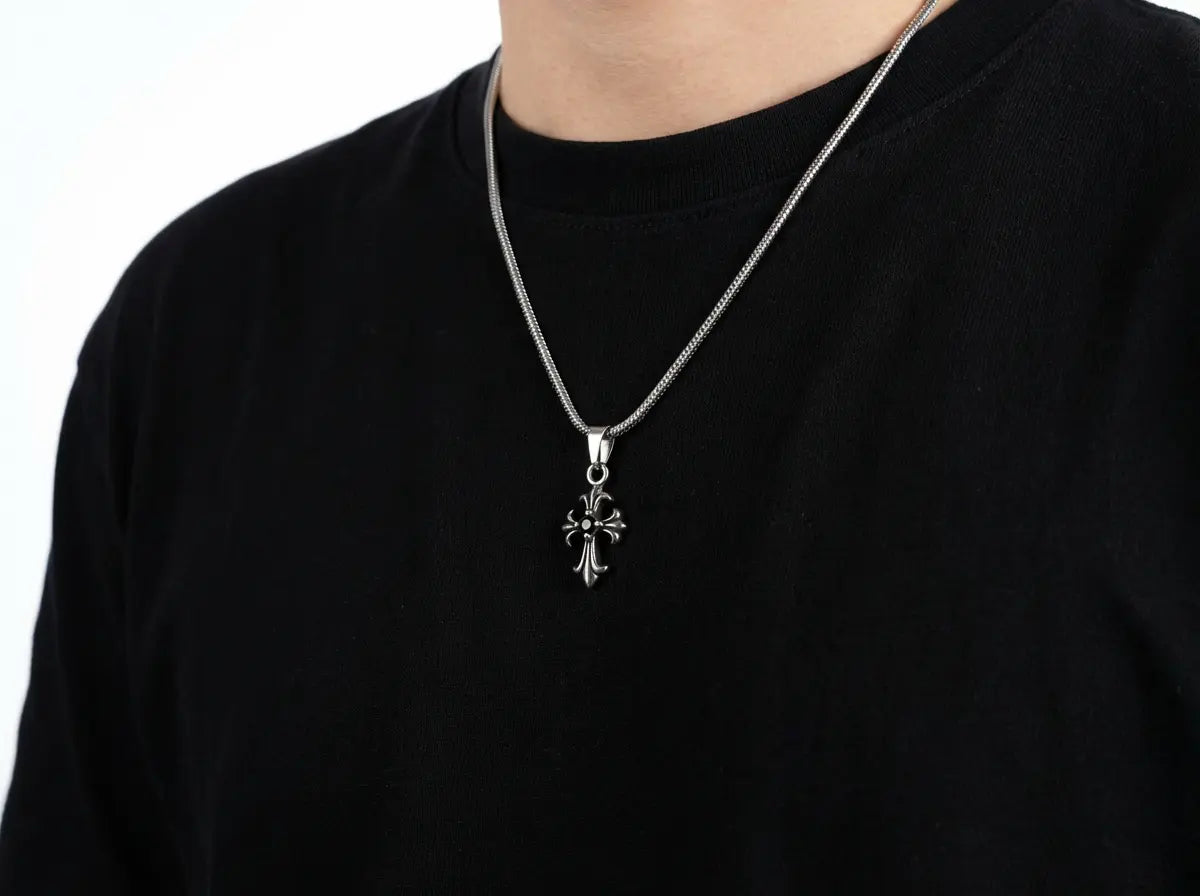 Person wearing a black shirt with a silver necklace featuring a cross pendant on a white background