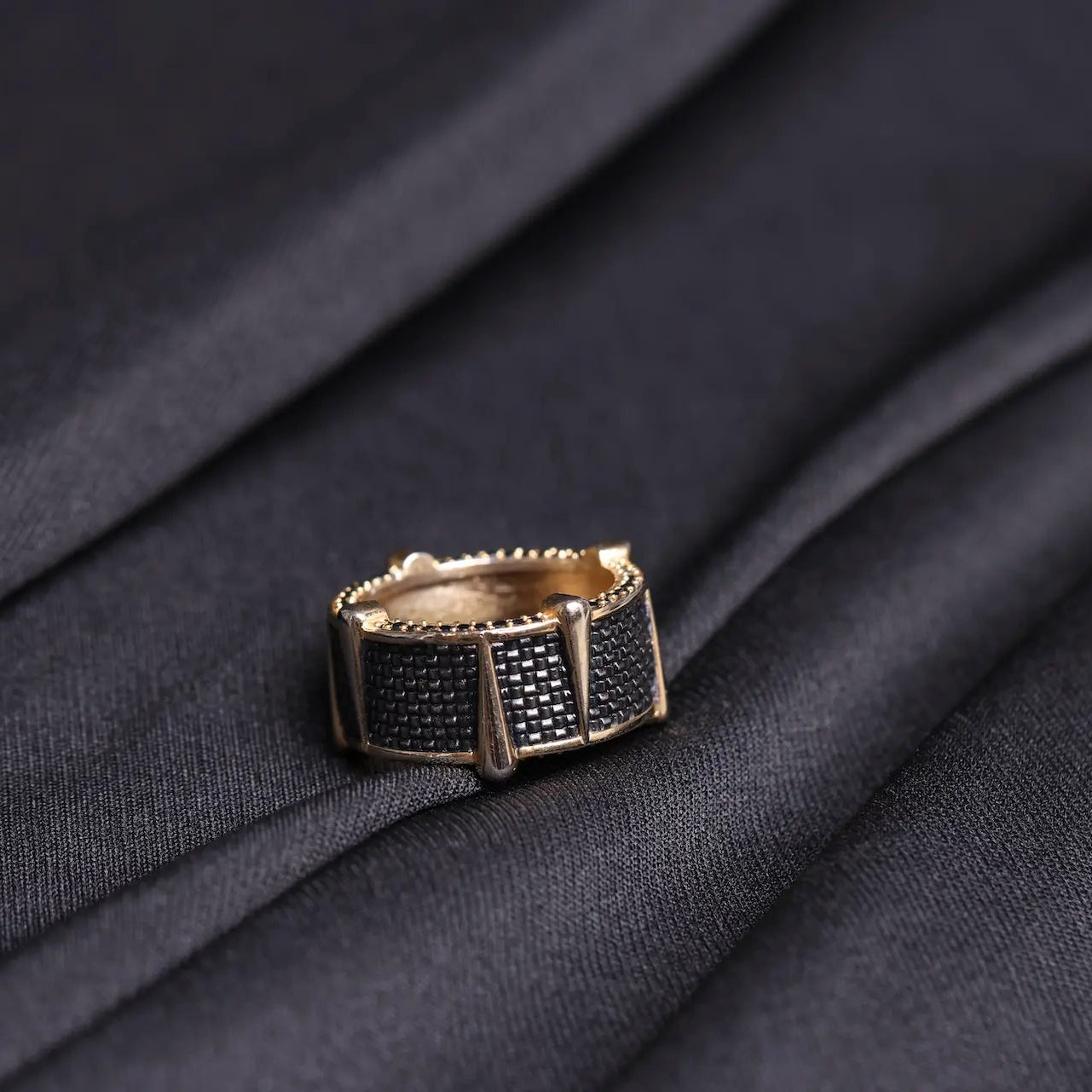 Gold ring with black gemstones on a dark fabric background