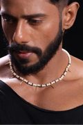 Man wearing Salitaire Spiked Pearl Necklace with gold spikes and freshwater pearls on black background